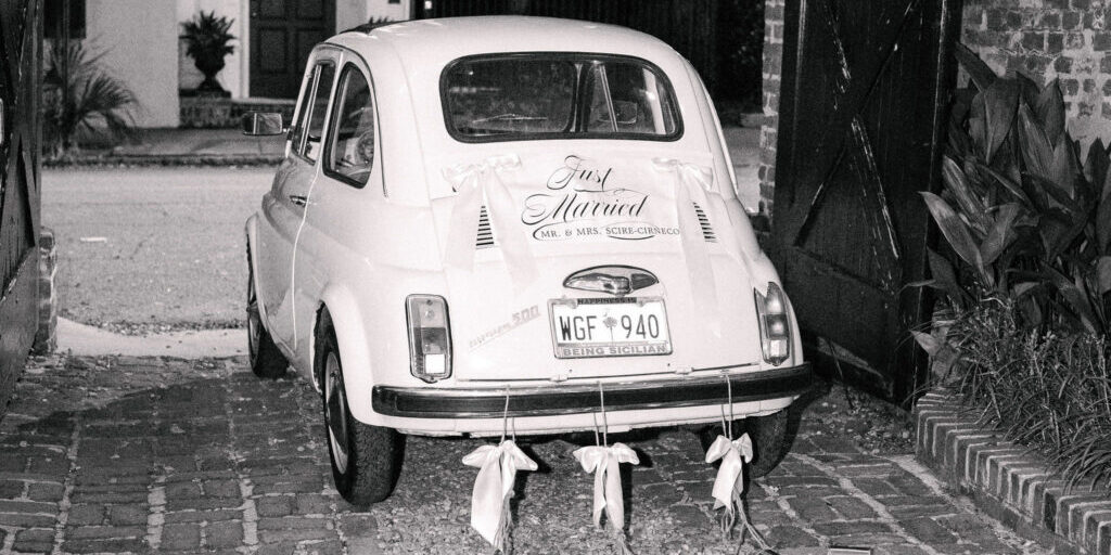 A small vintage car decorated with “Just Married” signage and tin cans trailing from the rear bumper.