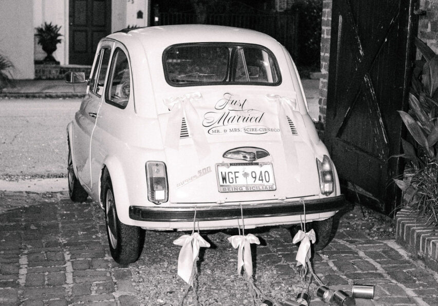 A small vintage car decorated with “Just Married” signage and tin cans trailing from the rear bumper.