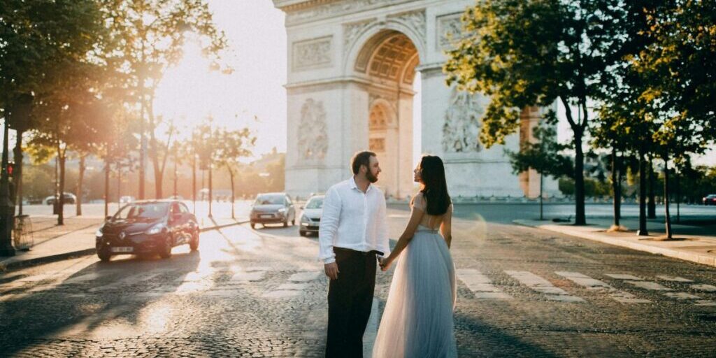 A couple holding hands while standing in front of the Arc de Triomphe in Paris.