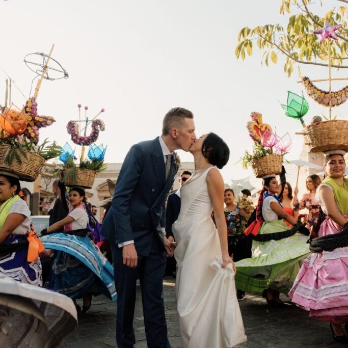 couple kissing as women in Mexican dresses twirl around them