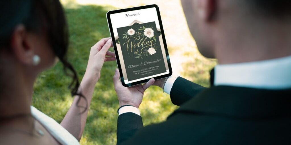 A couple holds a tablet displaying a digital wedding invitation with floral designs on a sunny day.