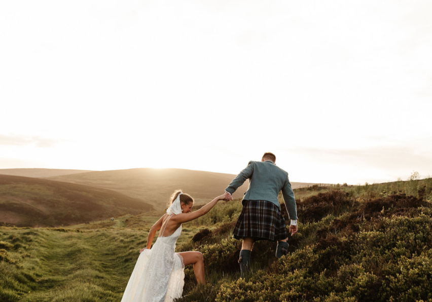 groom helps bride up hill in scottland