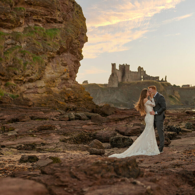 couple pose near ocean with Scottish castle in the background