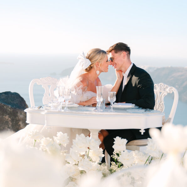 couple sitting at a table with flowers and greek coast backdrop