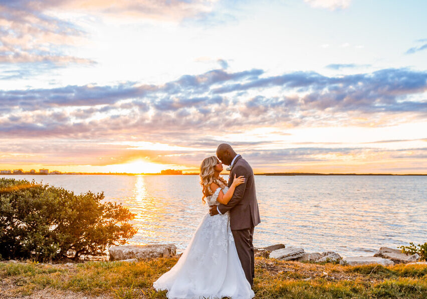 bride and groom pose at sunset by harbor